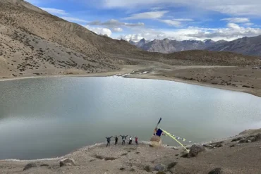 Panoramic view of the turquoise Dhankar Lake surrounded by the rugged, brown mountains of Spiti Valley under a clear blue sky.