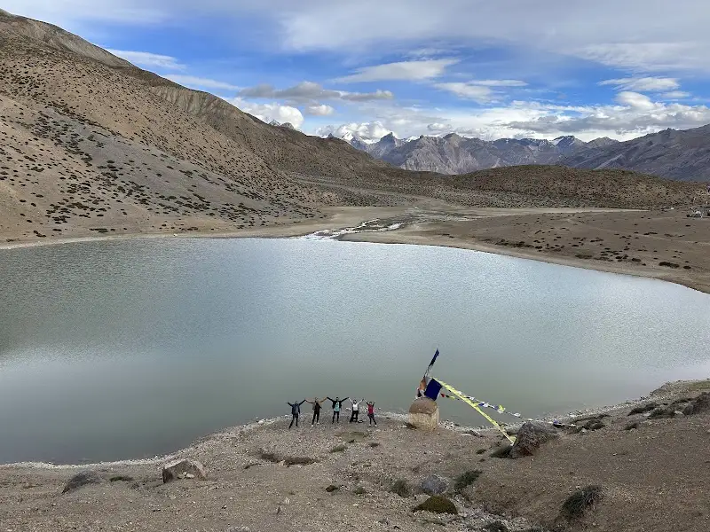 Panoramic view of the turquoise Dhankar Lake surrounded by the rugged, brown mountains of Spiti Valley under a clear blue sky.